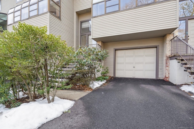 view of property exterior with an attached garage, stairs, and asphalt driveway