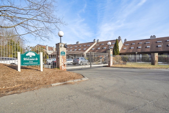 view of asphalt street with street lights, a gated entry, curbs, and a gate