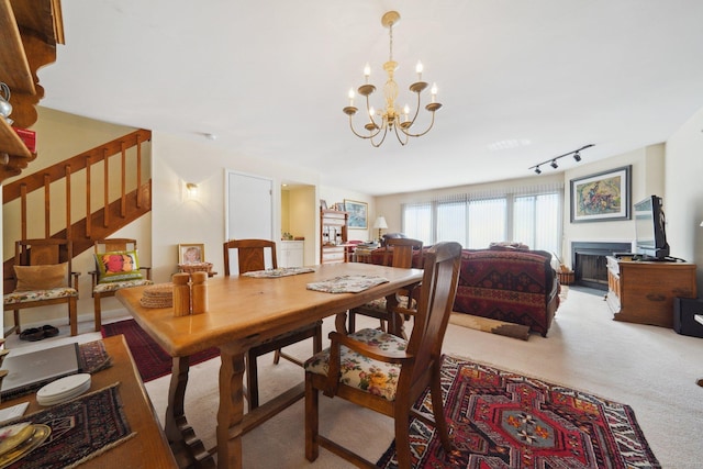 dining space featuring light colored carpet, stairway, a chandelier, and track lighting