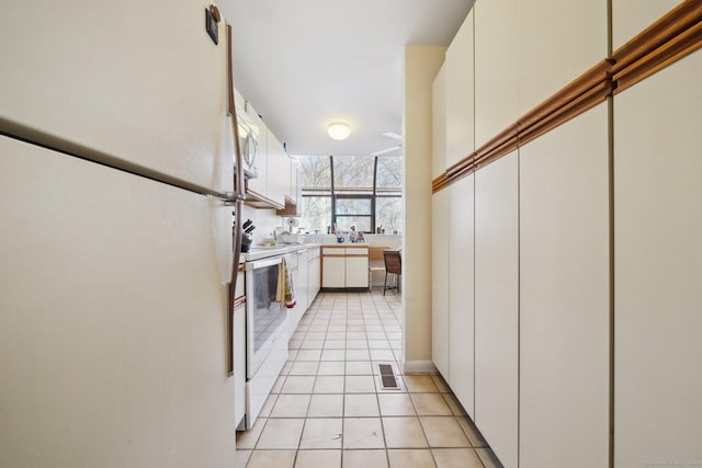 kitchen with white appliances, light tile patterned flooring, light countertops, white cabinetry, and a sink