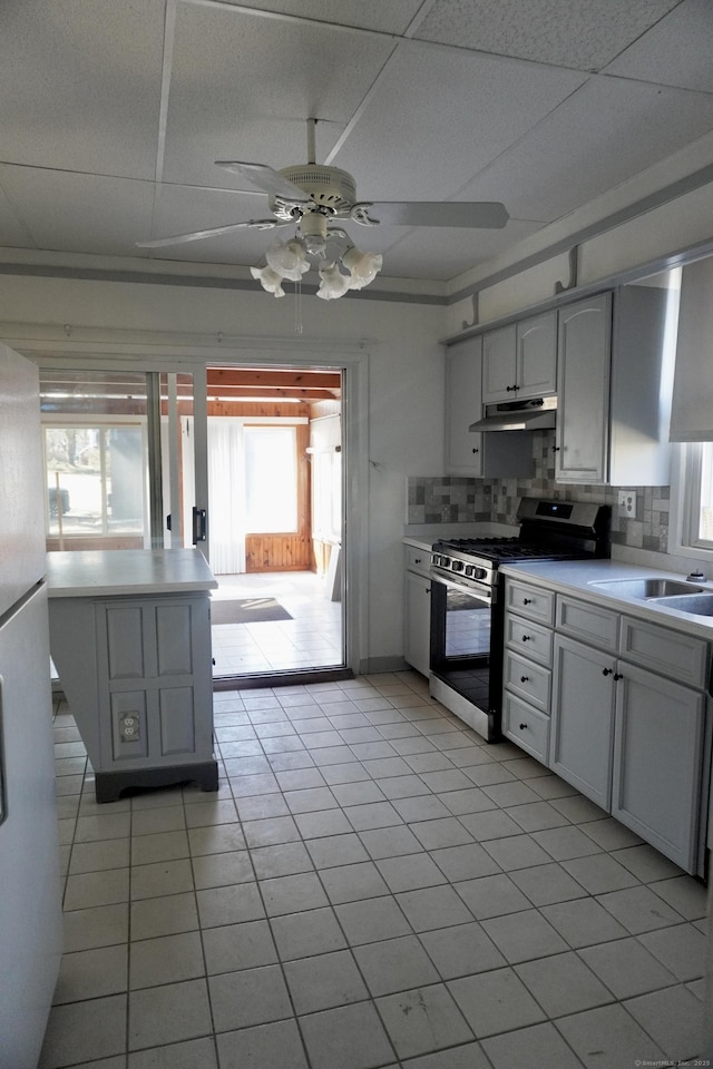 kitchen with a ceiling fan, under cabinet range hood, a sink, backsplash, and gas stove