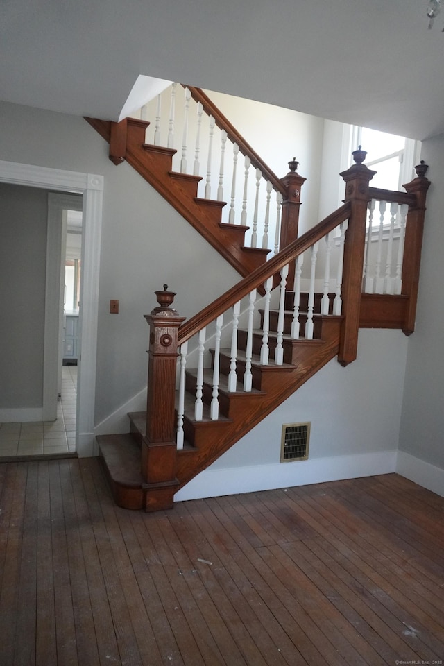 staircase with hardwood / wood-style floors, baseboards, and visible vents
