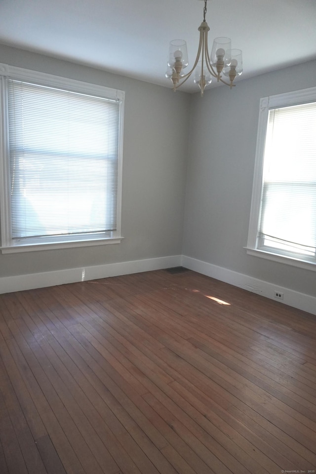 unfurnished room featuring baseboards, an inviting chandelier, and dark wood-style floors