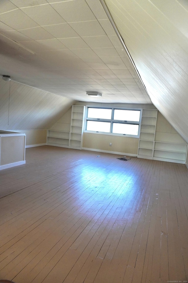 additional living space featuring built in shelves, lofted ceiling, and hardwood / wood-style floors