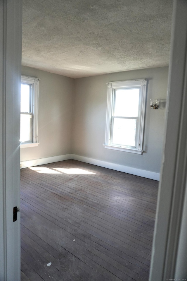 empty room with baseboards, wood-type flooring, and a textured ceiling