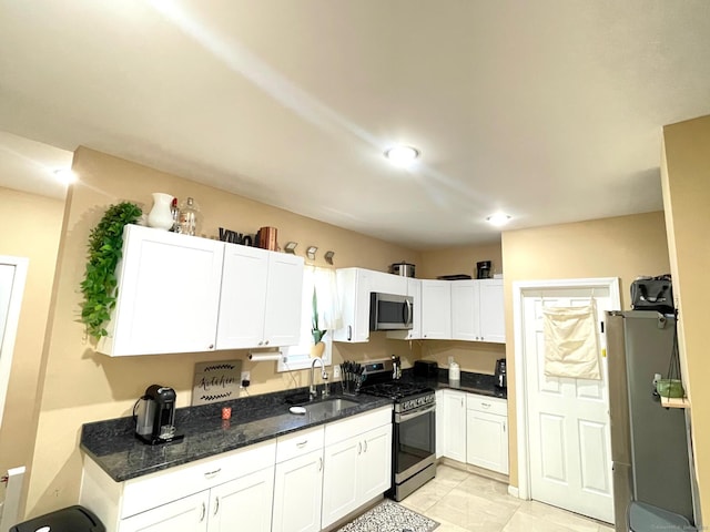 kitchen with a sink, stainless steel appliances, dark stone counters, white cabinets, and light tile patterned floors