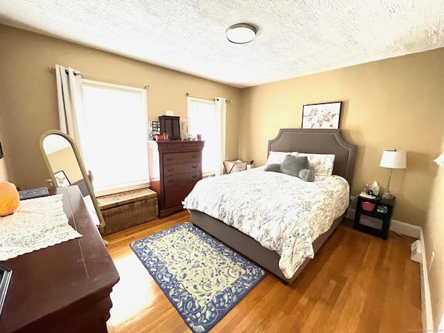 bedroom with a textured ceiling, baseboards, and wood finished floors