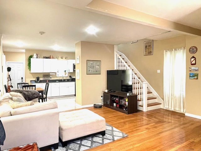 living area with light wood-type flooring, stairway, and baseboards