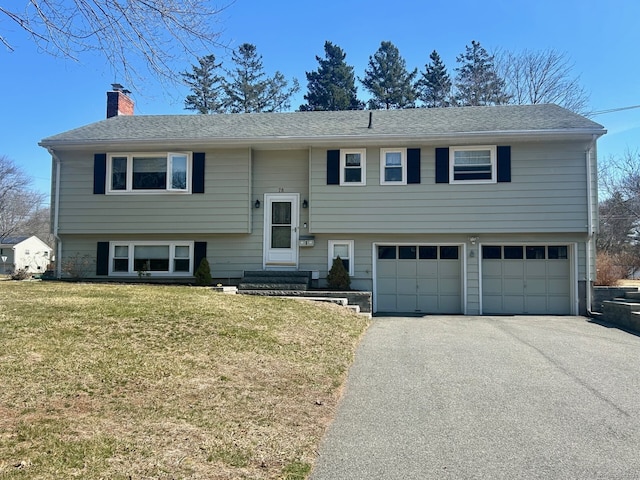 bi-level home with a front yard, an attached garage, a shingled roof, a chimney, and aphalt driveway