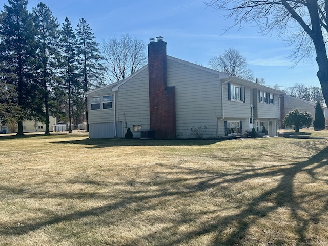 view of side of property with central AC unit, a chimney, and a yard