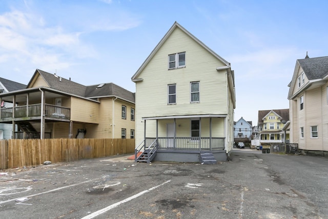 rear view of property with a residential view, covered porch, uncovered parking, and fence