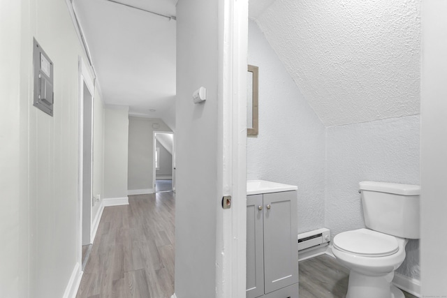 half bathroom with baseboard heating, wood finished floors, vanity, and toilet