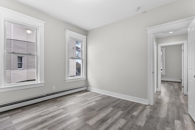 empty room with a baseboard radiator, baseboards, baseboard heating, and wood finished floors