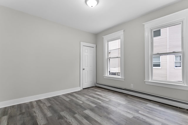 spare room with a baseboard heating unit, baseboards, and wood finished floors