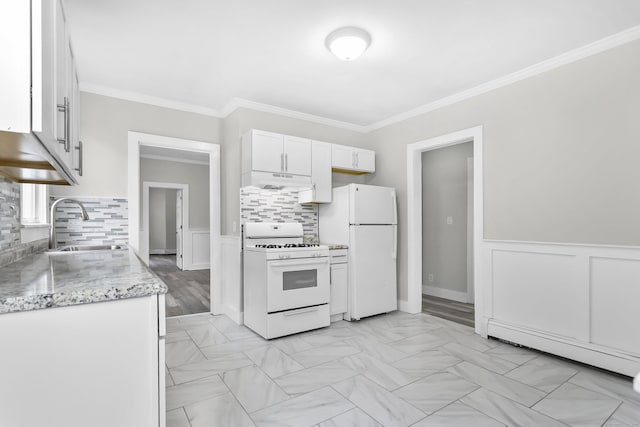 kitchen with under cabinet range hood, ornamental molding, wainscoting, white appliances, and a sink