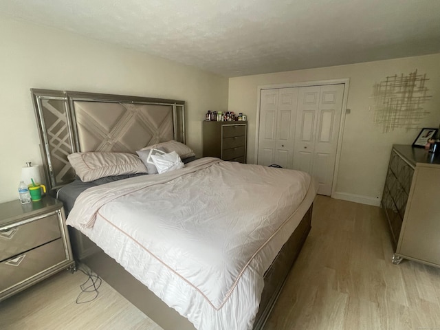 bedroom with baseboards, light wood-type flooring, and a closet
