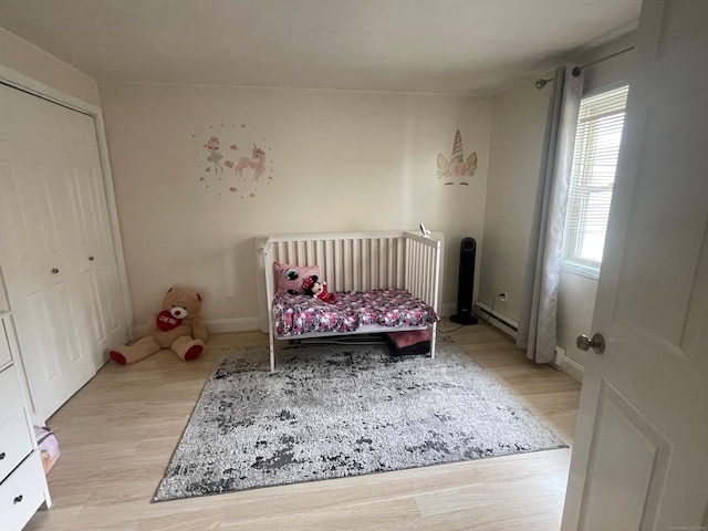 bedroom with a baseboard heating unit, light wood-style floors, and baseboards