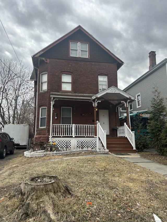view of front facade with brick siding, covered porch, and a front lawn