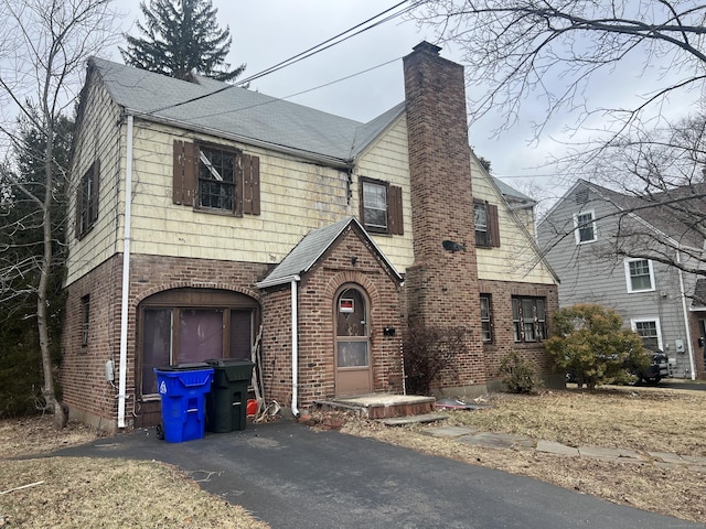 view of front of property featuring brick siding, driveway, and a chimney