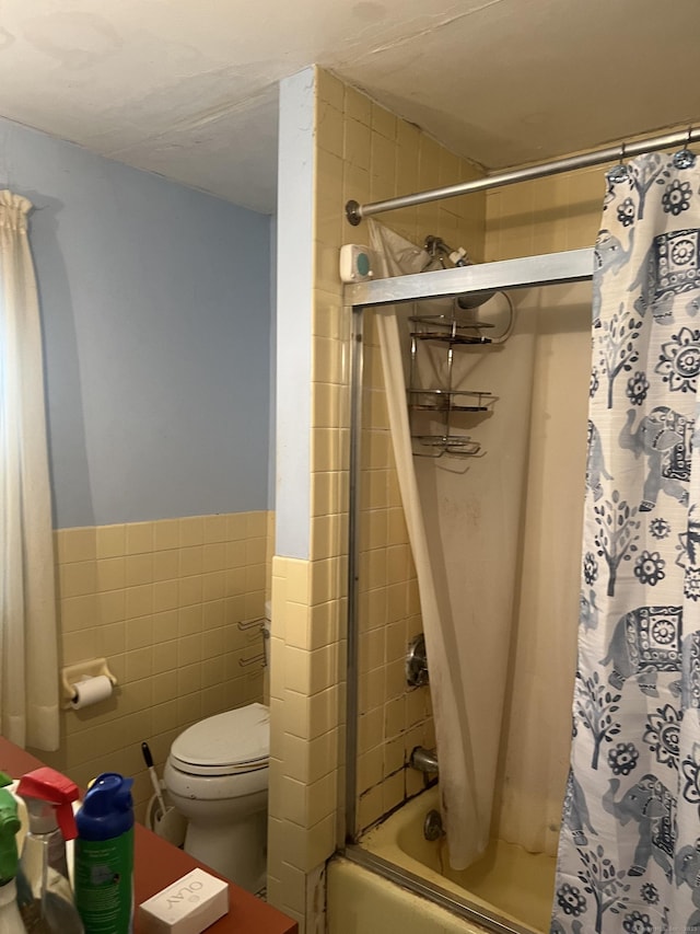 bathroom featuring tile walls, toilet, shower / tub combo with curtain, and wainscoting