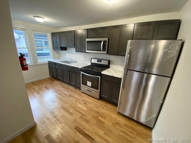 kitchen with baseboards, stainless steel appliances, light wood-style floors, and a sink