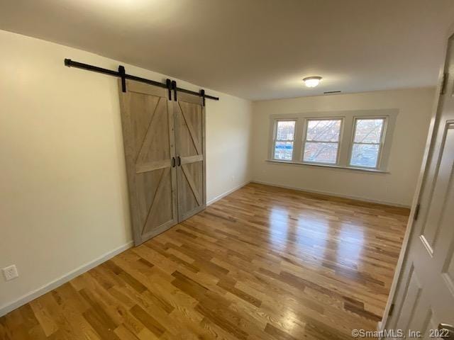 empty room featuring a barn door, wood finished floors, and baseboards