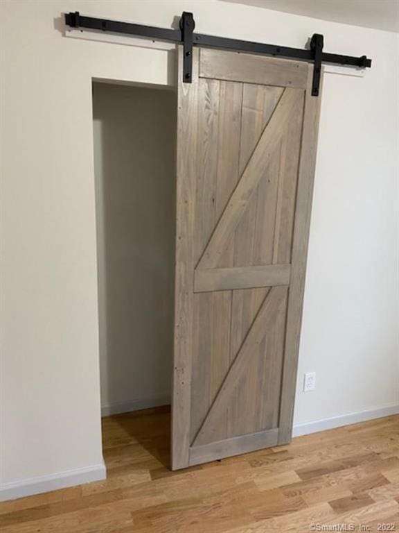 room details featuring a barn door, wood finished floors, and baseboards