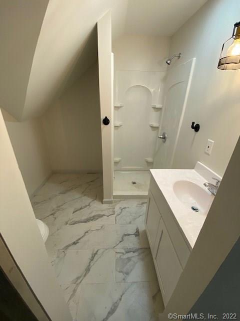 full bathroom with toilet, marble finish floor, a shower stall, lofted ceiling, and vanity