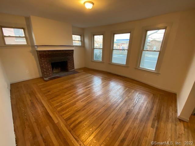 unfurnished living room featuring baseboards, a brick fireplace, and wood finished floors