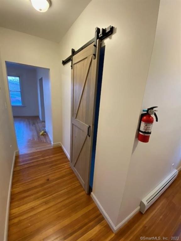 hallway featuring baseboards, light wood-type flooring, a baseboard heating unit, and a barn door