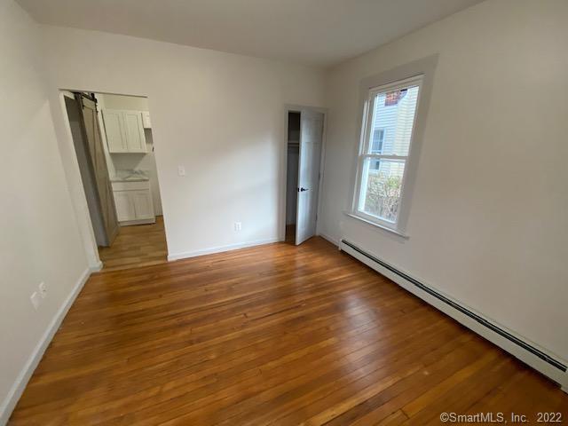 unfurnished bedroom with a barn door, baseboards, a baseboard heating unit, and light wood-style floors