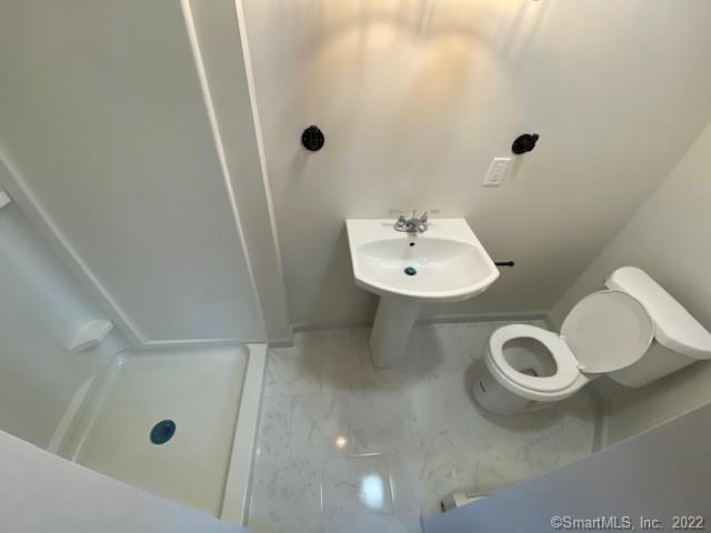 bathroom featuring toilet, marble finish floor, and a stall shower