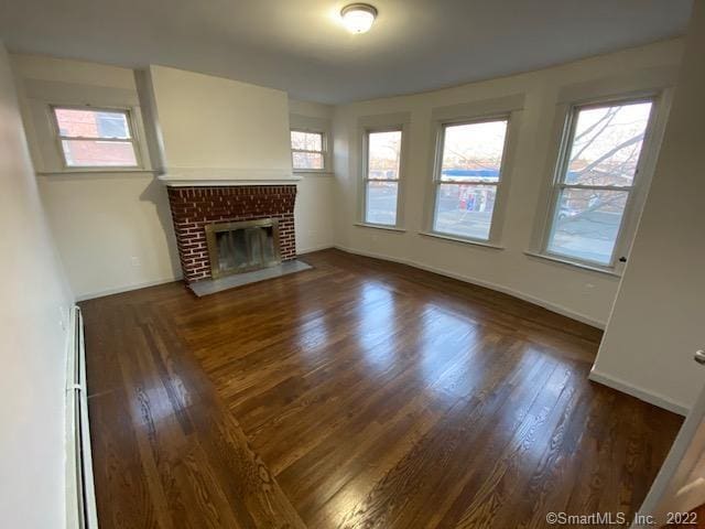 unfurnished living room featuring a baseboard radiator, baseboards, a brick fireplace, and wood finished floors