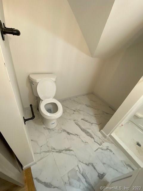 bathroom featuring lofted ceiling, toilet, and marble finish floor