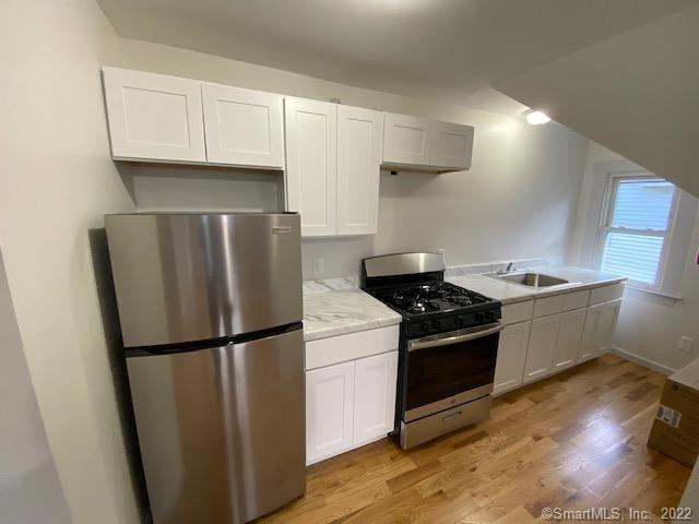 kitchen featuring a sink, appliances with stainless steel finishes, white cabinets, and light wood finished floors