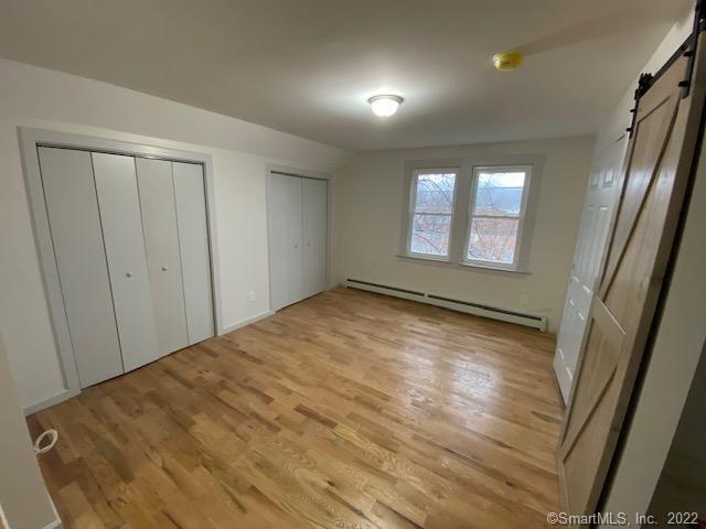 unfurnished bedroom with a barn door, two closets, a baseboard heating unit, and light wood finished floors