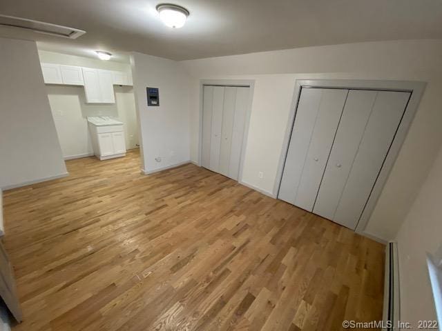 unfurnished bedroom with a baseboard heating unit, two closets, and light wood-type flooring