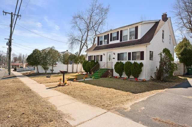 colonial inspired home featuring a shingled roof, a chimney, and fence