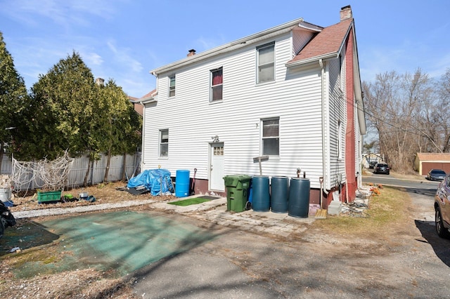 rear view of house featuring a chimney and fence