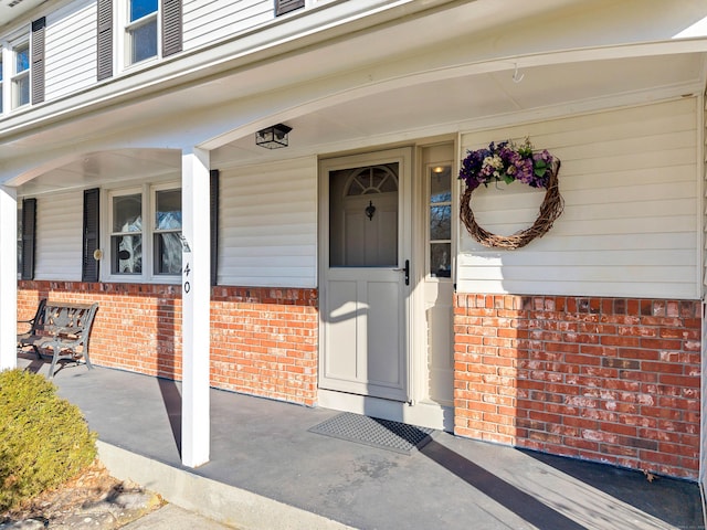 doorway to property with brick siding and a porch