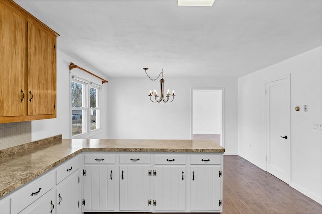 kitchen with wood finished floors, a peninsula, light countertops, decorative light fixtures, and a notable chandelier