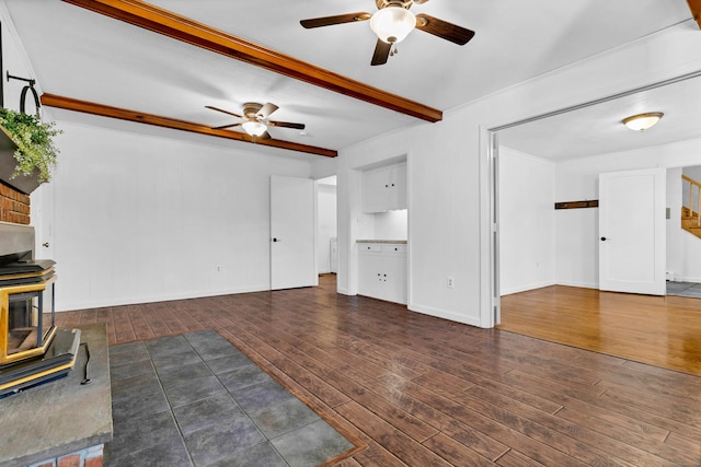 unfurnished living room with baseboards, beam ceiling, a wood stove, ceiling fan, and wood-type flooring