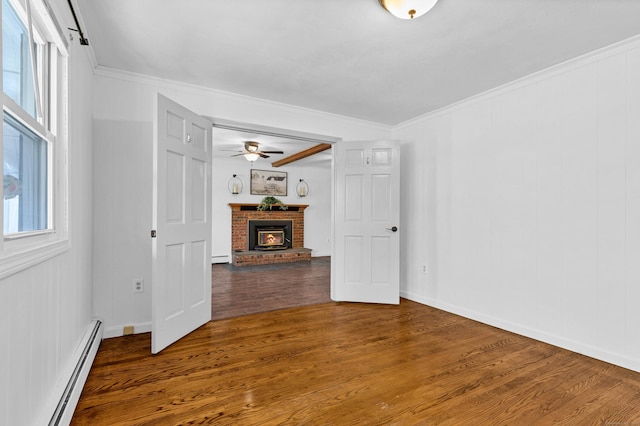 spare room featuring crown molding, a brick fireplace, wood finished floors, and baseboard heating