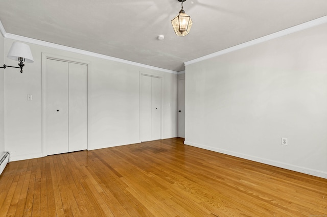 unfurnished bedroom with hardwood / wood-style flooring, baseboards, multiple closets, and ornamental molding