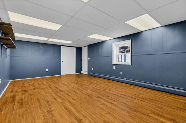 below grade area with wood finished floors, a drop ceiling, and a baseboard radiator