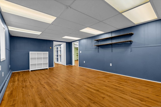 unfurnished room featuring a drop ceiling, wood finished floors, and a baseboard radiator