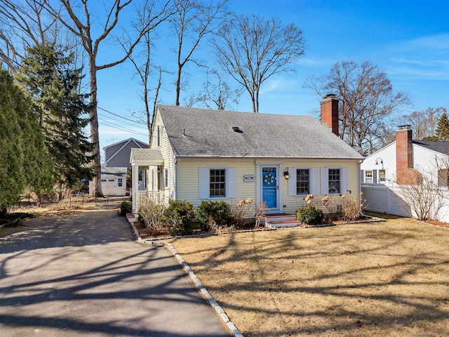 view of front facade with driveway, a front lawn, fence, a shingled roof, and a chimney