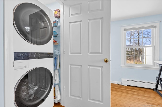 laundry area featuring wood finished floors, baseboards, a baseboard radiator, stacked washing maching and dryer, and laundry area