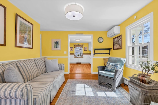 living room with baseboard heating, an AC wall unit, baseboards, and wood finished floors