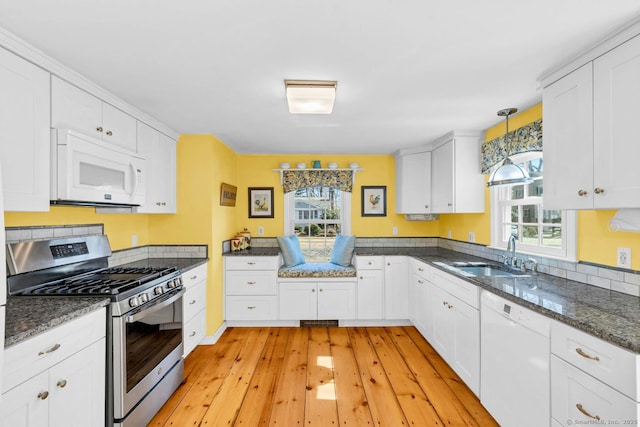 kitchen featuring a sink, dark stone countertops, white cabinetry, white appliances, and light wood-style floors